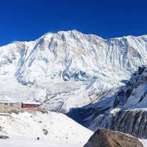 Snow-covered Annapurna Sanctuary with mountain lodges in the foreground, under a clear blue sky