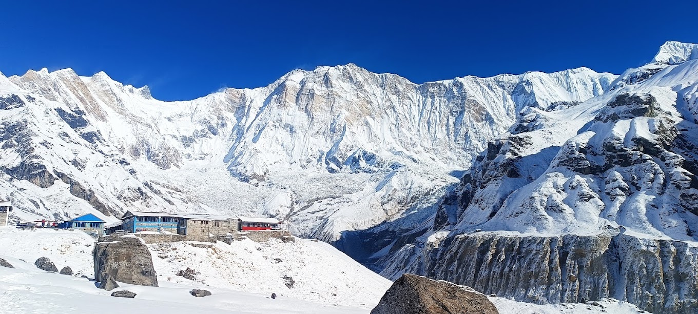 Snow-covered Annapurna Sanctuary with mountain lodges in the foreground, under a clear blue sky