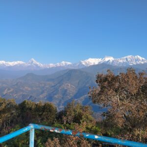 Panoramic view of the Annapurna mountain range from a lookout point during the Royal Trek in Nepal, with clear blue skies and lush greenery in the foreground.