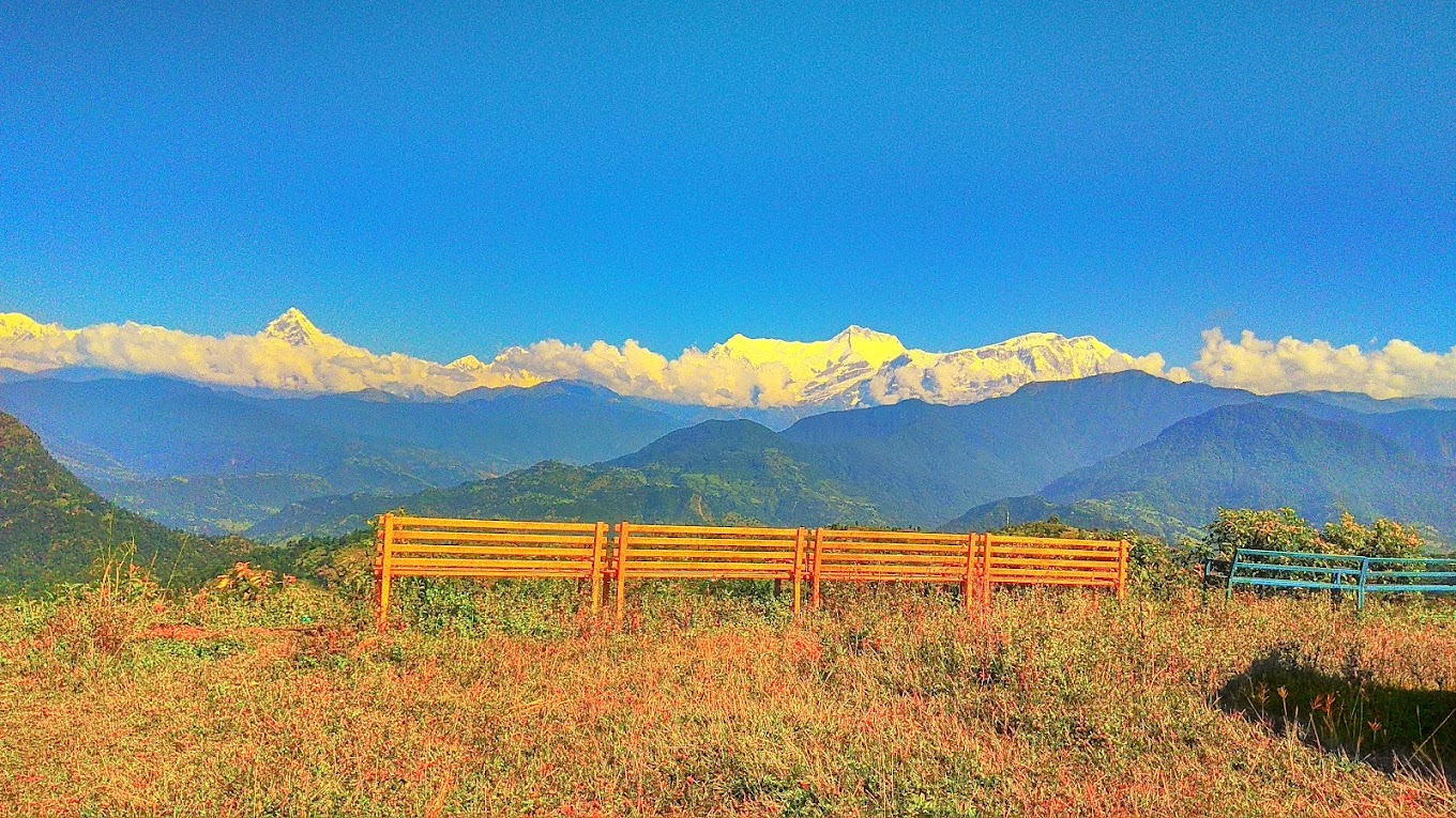 Stunning panoramic view of the Annapurna mountain range from Begnaskot, Nepal, with vibrant green hills and clear blue skies in the background.