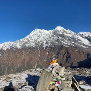 Stone cairn with prayer flags against the backdrop of snow-capped peaks on the Mardi Himal Trek in Nepal, under a clear blue sky.