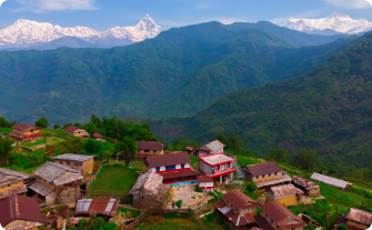 A scenic rural village in Pokhara, Nepal, with traditional houses surrounded by lush green hills and the snow-capped Himalayan mountains in the background.