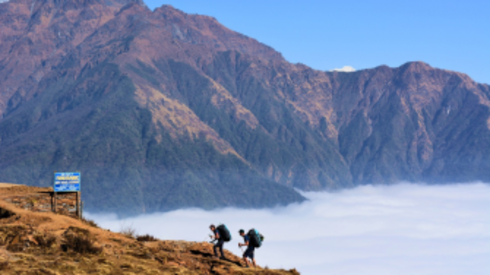 Two hikers trekking above the clouds in Nepal's Annapurna region, with towering mountains in the background during the Royal Trek.