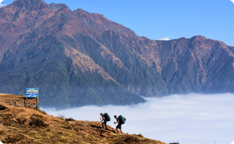 Two hikers trekking above the clouds in Nepal's Annapurna region, with towering mountains in the background during the Royal Trek.