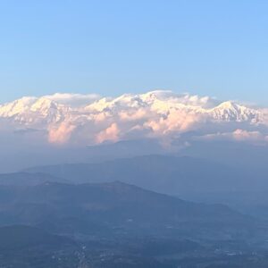 Distant view of the Himalayan mountain range with snow-capped peaks illuminated by the soft light of sunrise, set against a clear blue sky.