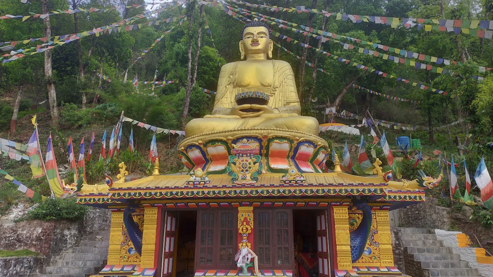 Golden Buddha statue at a vibrant monastery in Pokhara, Nepal, surrounded by colorful prayer flags and lush green trees, representing a key site on the Pokhara Buddhist Circuit.